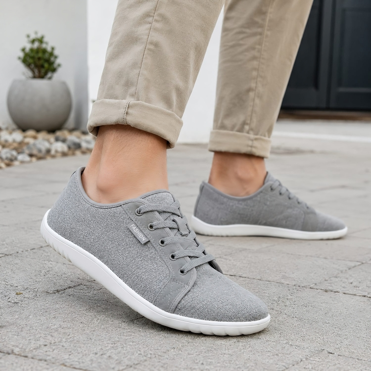 Grå barfotaskor unisex burna utomhus på stenbelagd yta med beige chinos