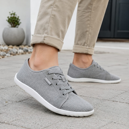 Grå barfotaskor unisex burna utomhus på stenbelagd yta med beige chinos
