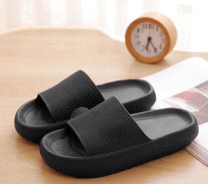 Svarta ergonomiska tofflor med tjock stöddämpande sula på träbord hemma – bekväma tofflor för vardag och återhämtning