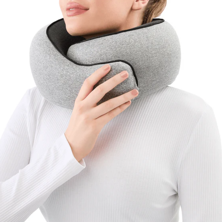 Kvinna bär grå resekudde runt nacken och justerar passformen med ena handen, visar ergonomiskt nackstöd framifrån