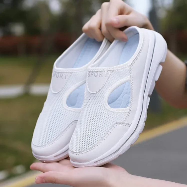Person håller upp ett par vita slip-on skor utomhus, sedda underifrån mot sulan